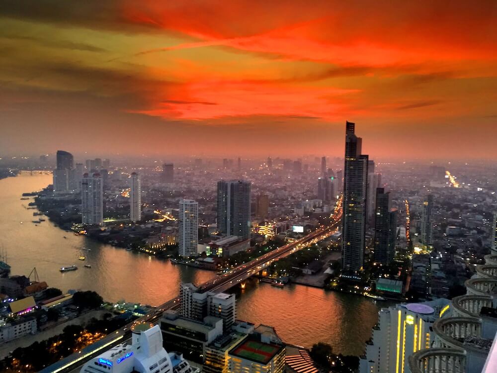 Bangkok Skyline bei Sonnenuntergang mit orangefarbenem Himmel über dem Fluss.